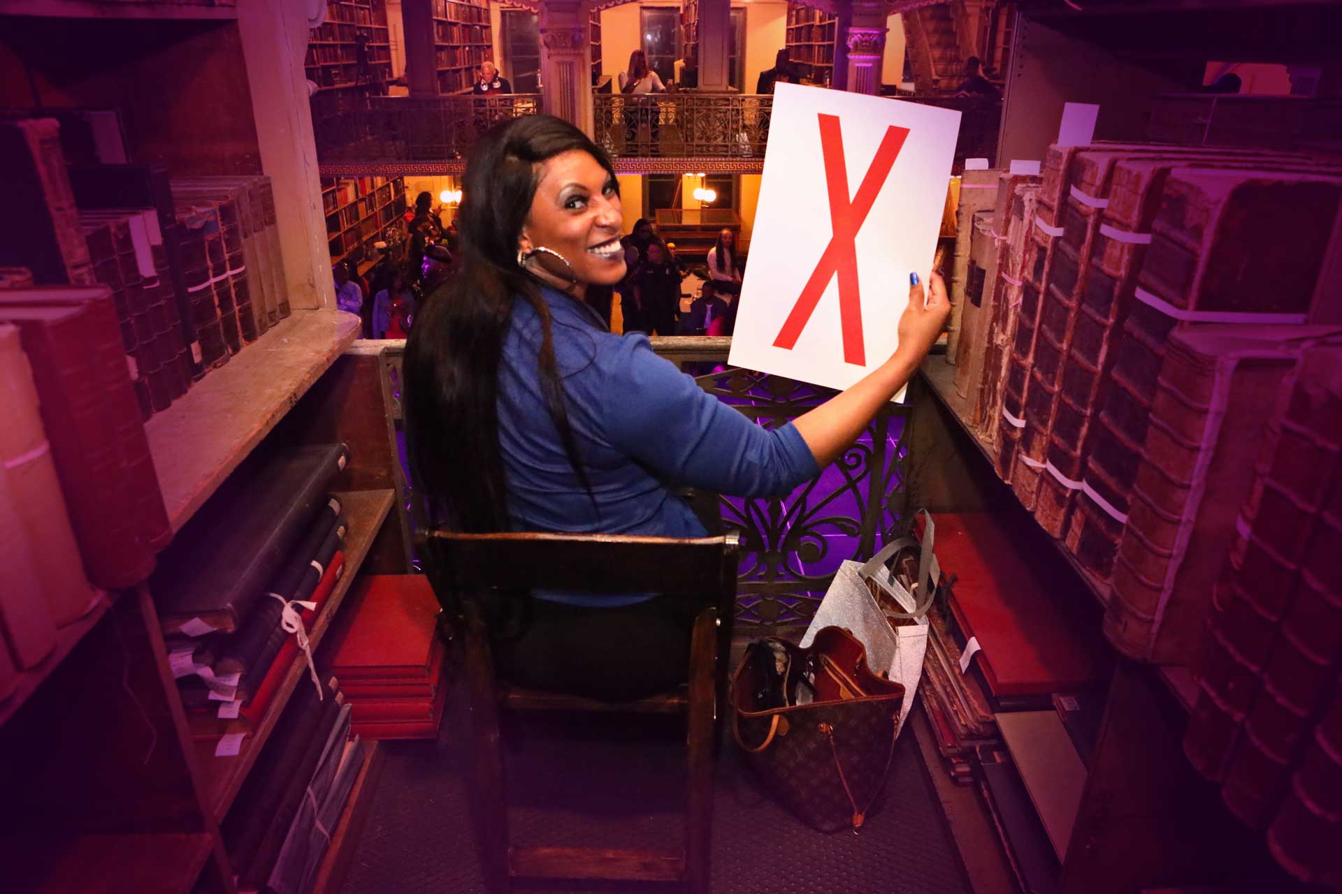 A person in between books holding an "X" poster
